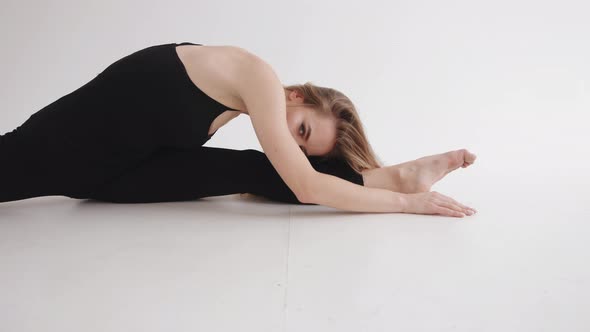 A Young Girl with a Beautiful Makeup in a Stretching Studio Sits on a Transverse Twine and Bends