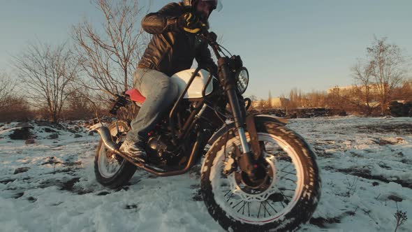 Professional Motorcyclist Drift and Turns on a Motorcycle on the Snow Ground at Sunset