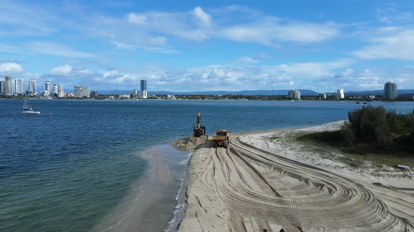 Moving drone view of heavy machinery working on a coastal rejuvenation project with a city skyline i