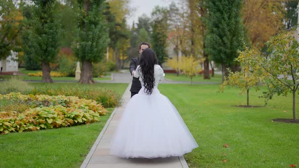 Groom and His Young Beautiful Bride are Walking in Garden in Autumn Day After Wedding Ceremony