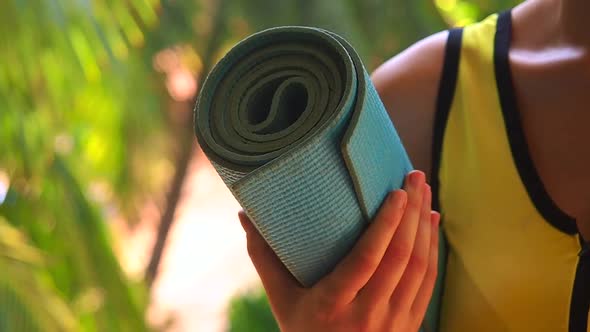 Young Woman Holding Roll Yoga Mat Outside in Natural Environment