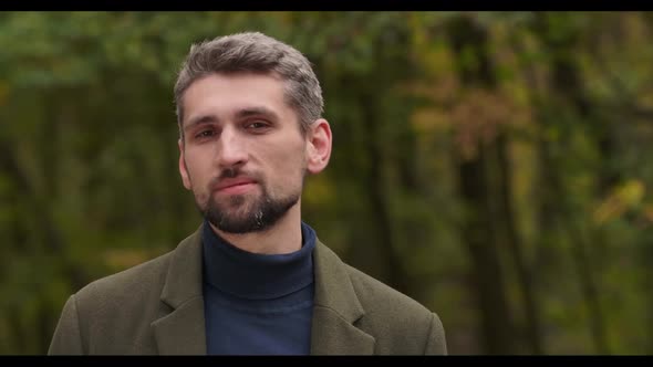 Close-up Face of Smiling Handsome Gray-haired Caucasian Man with Brown Eyes Standing in Forest