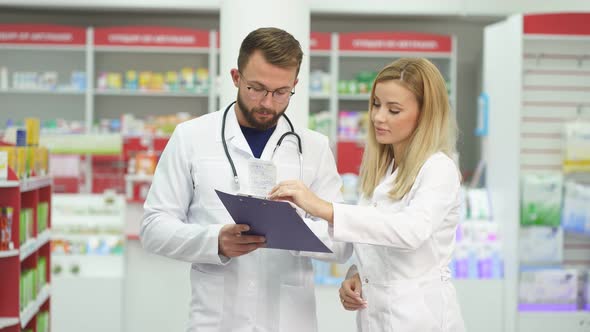 Appealing Two Caucasian Pharmacists Communicating While Supervising Medical Products