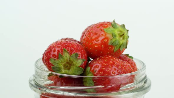 Glass jar with red ripe strawberries rotating counterclockwise on a white background.