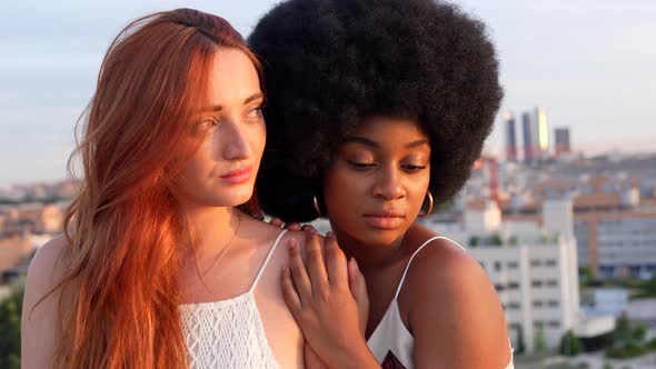 Female couple snuggling in city at sunset