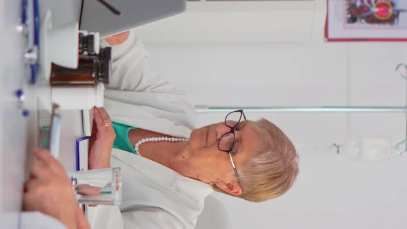 Vertical Video Elderly Specialist Doctor in Lab Coat Typing on Laptop and Smiling at Camera