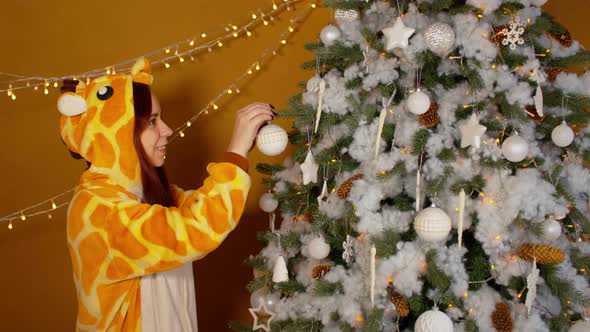 Woman in costume of giraffe decorating and hanging baubles on Christmas tree.