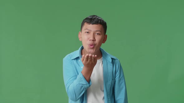 Portrait Of A Smiling Young Asian Boy Blowing Kisses To A Camera In The Green Screen Studio