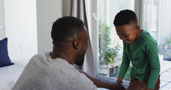 African american father helping his son with getting dressed in bedroom