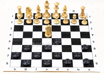 lack checkers and white chess figures on black white chessboard, above view of non-standard knight move (focus on the knight)