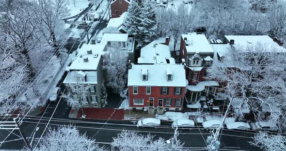 Brick home with light on at night during winter snow flurries. Descending aerial in USA town.