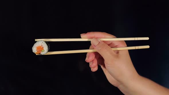 Woman Holding Maki Sushi with Chopsticks in Dark