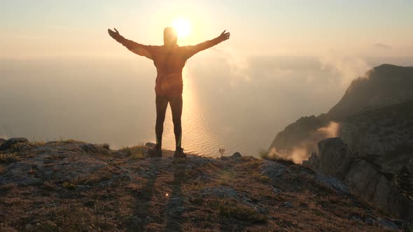 Filming From the Back of an Active Man Standing on the Edge of the Mountain and Spreading His Arms