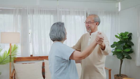 Asian active senior couple, grandfather and grandmother enjoy dancing together in living room