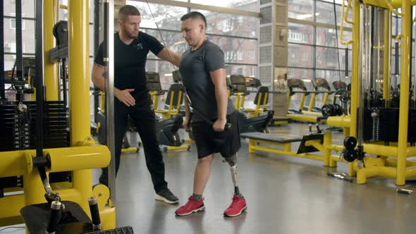 Disabled Young Man with Instructor Working Out in Gym