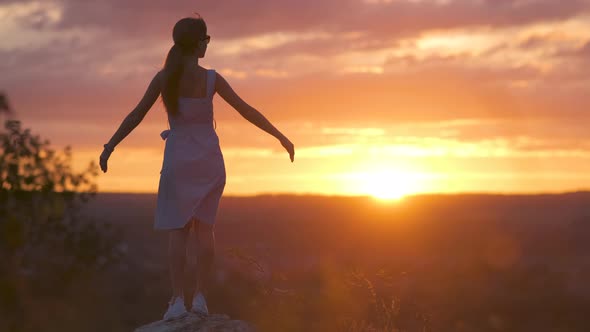 Dark Silhouette of a Young Woman Standing with Raised Up Hands on a Stone Enjoying Sunset View