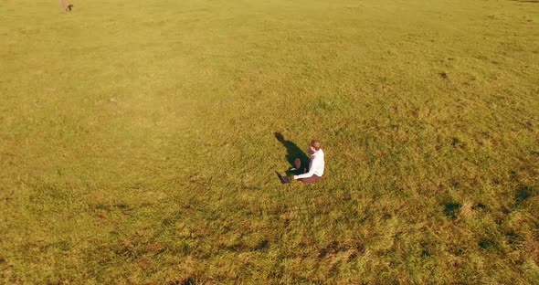 Low Orbital Flight Around Man on Green Grass with Notebook Pad at Yellow Rural Field