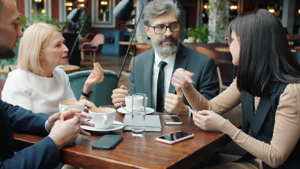 Businessmen and Businesswomen Speaking in Cafe Discussing Work Gesturing