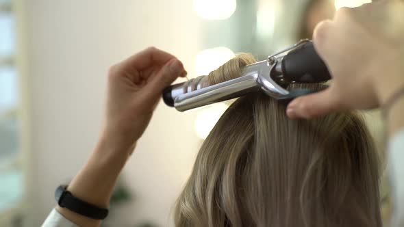 Closeup View of Hairdresser Making Hairstyle Using Curling Tongs for Long Hair