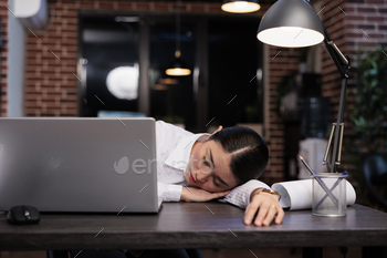 k because of overtime working hours at night. Exhausted agency worker falling asleep in office workspace while working on project.