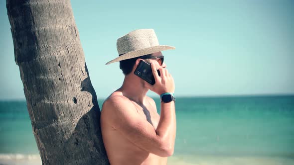 Man Sitting On Palm And Talking On Smartphone On Vacation Lounge Sea. Man Resting On Ocean.