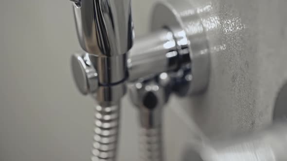 Closeup Camera Tilting Up Over Shiny Stainless Hose and Small Showerhead Hanging on Tiled Wall in