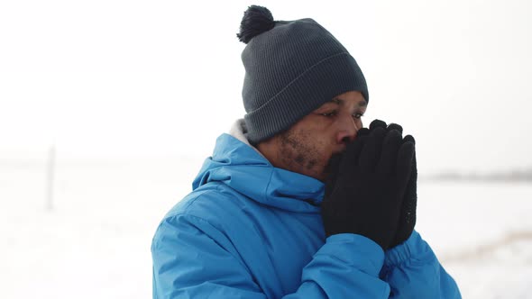 Black Man in Winter Clothes Warm Gloved Hands with His Breath and Starts Jogging Front View