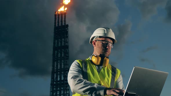 Petroleum Expert is Operating a Laptop Near the Flare Stacks