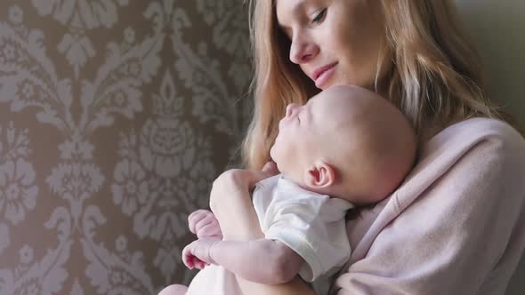 Newborn Baby Sleeps Tightly in His Mother's Arms. Mom Carefully Caresses Her Baby in Her Arms and