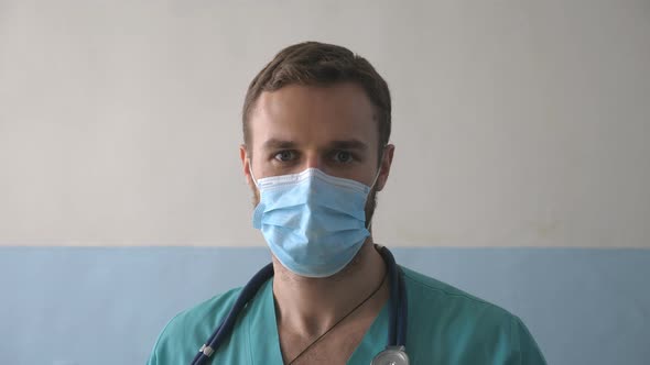 Portrait of Young Male Caucasian Doctor with Medical Face Mask Looks at Camera. Medical Worker