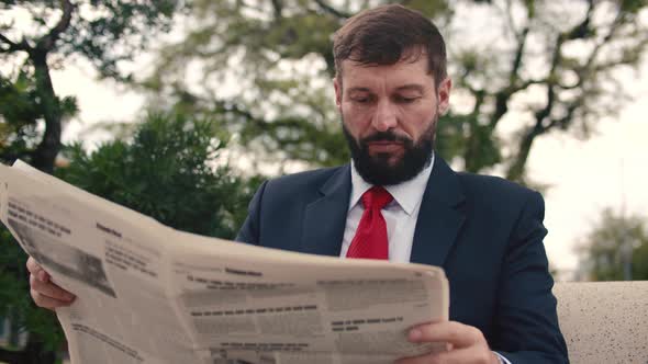 Businessman Senior in an Expensive Suit with a Beautiful Beard in Black Blue Jacket Sits on Bench in