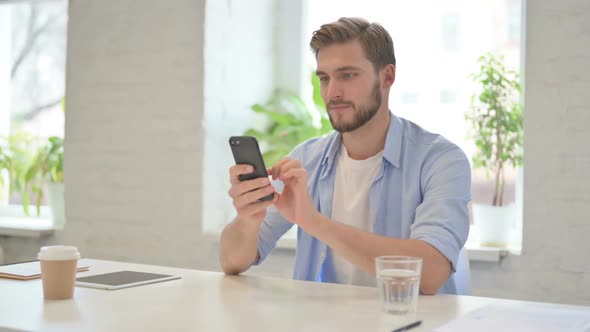 Attractive Young Creative Man Using Smartphone in Modern Office