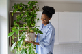 Happy pleased young African woman holding potted Philodendron plant enjoying home gardening - PhotoDune Item for Sale