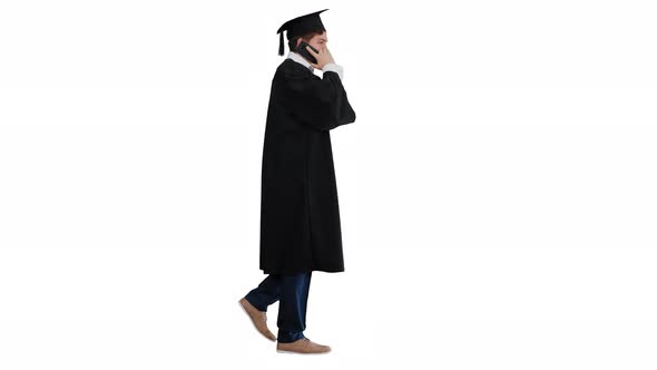 Smiling Male Student in Graduation Robe Walking and Making a Call on White Background