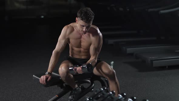 Athletic Man Trains in the Gym Lifts Dumbbells and Performs Hand Exercises Cinematic Light