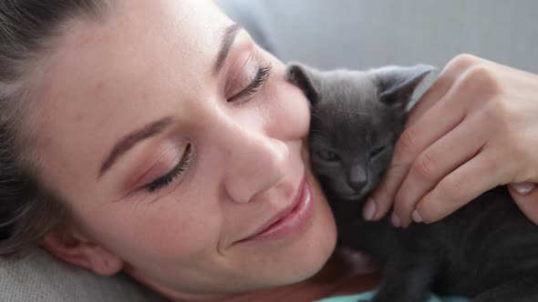 Smiling Woman Lying on Couch Cuddling Tiny Kitten