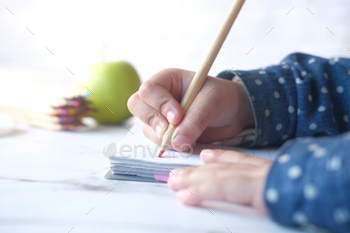 Close up of a child hand drawing with colored pencil on a page.