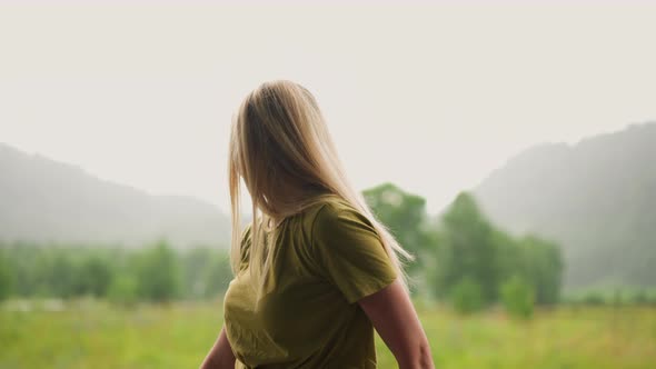 Pretty Woman with Blonde Hair Looks Around at Lush Field