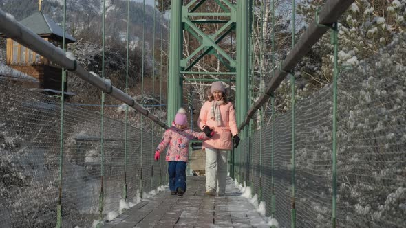 Woman with Daughter Walking on Suspension Bridge