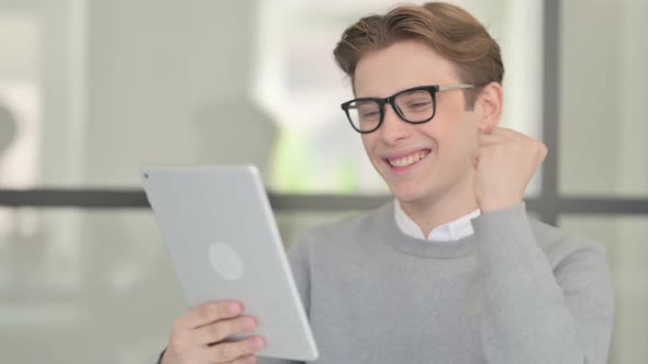 Young Man Celebrating on Tablet in Modern Office