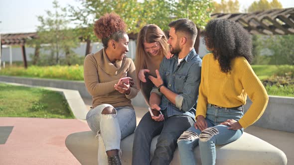 Four multinational young friends chatting and laughing in the park