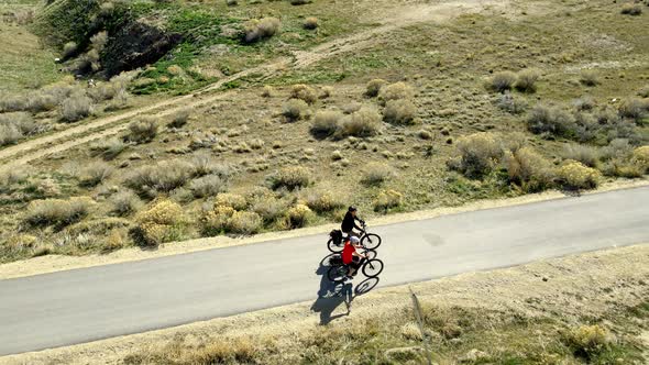 Husband and wife couple riding bicycles along a paved path in a desert landscape - aerial view