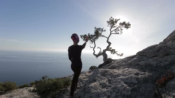 Young Woman Looks on the Sun Beams Through Branches of a Pine on a Mountain Above Black Sea in