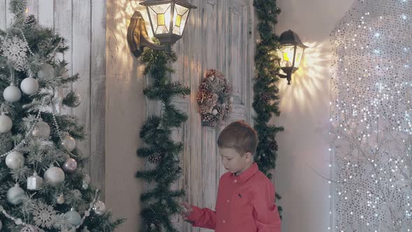 Schoolboy in Red Shirt Touches Pine Garland Decor in Room