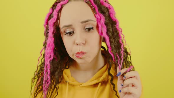 Young Woman Twists Hair with Thoughtful Look on Yellow Background