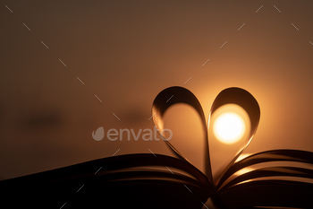 Open book with heart-shaped pages against a beautiful sunset