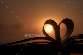 Open book with heart-shaped pages against a beautiful sunset