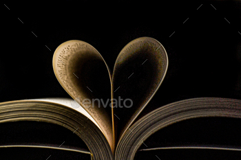 Closeup of an open book with the pages forming a heart on the black background