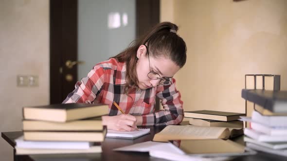 girl prepares for exams by reading and taking notes. She is sitting at a table