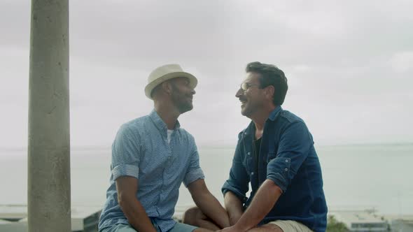 Front View of Gays Sitting on Background of Sea and Kissing